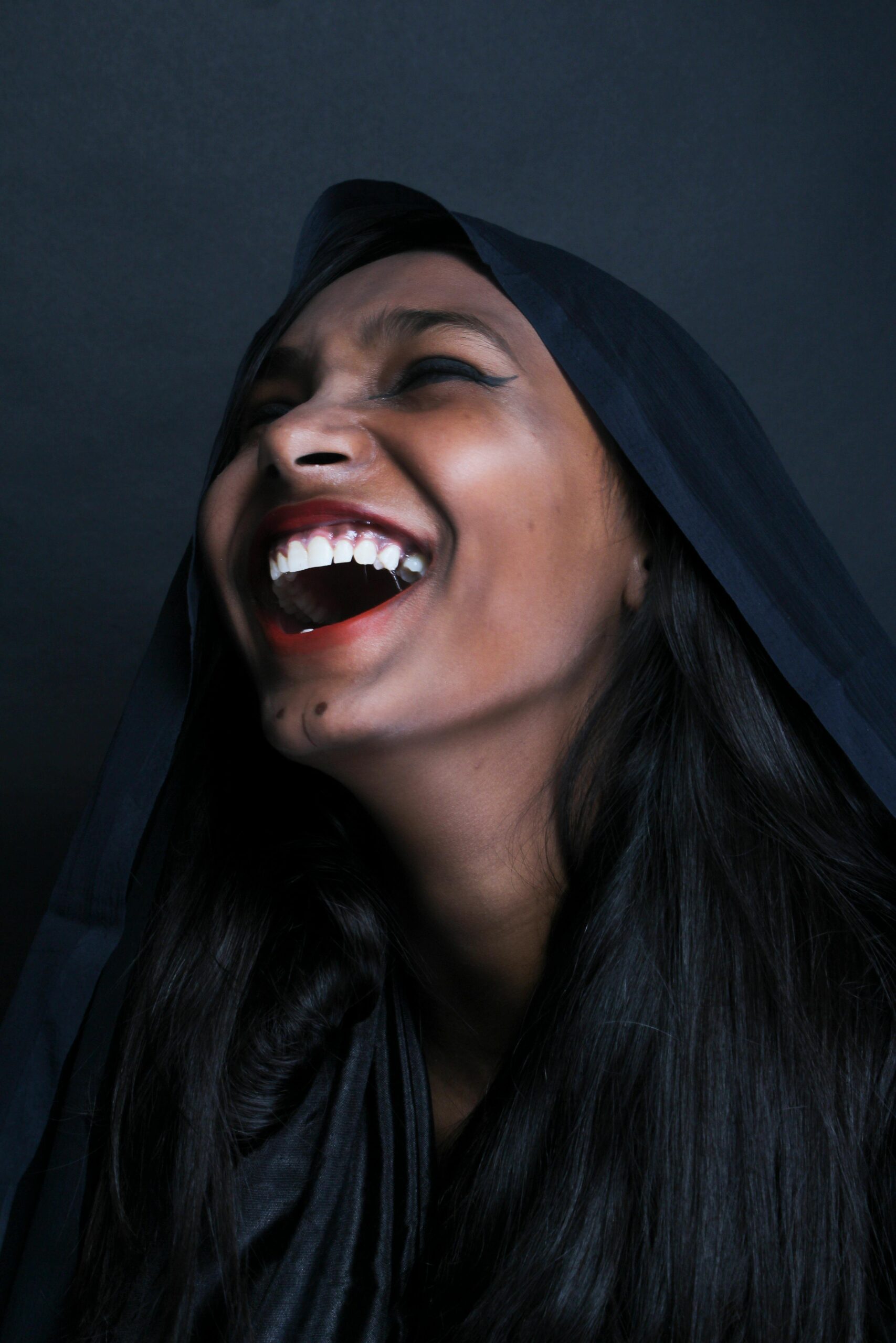 A joyful portrait of a woman with black hair laughing in a hood, showcasing elegance and happiness.